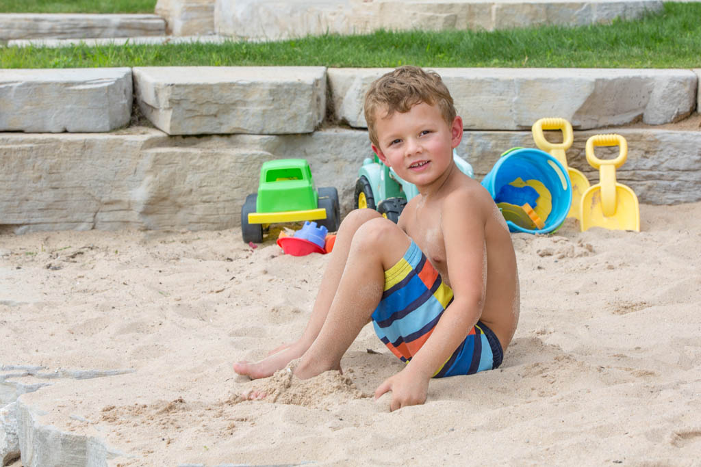 boy sitting in the sand with a green plastic toy tractor